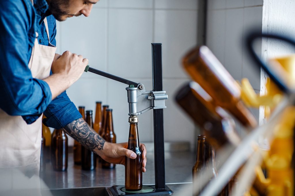 Man putting caps on beer bottles with a tool